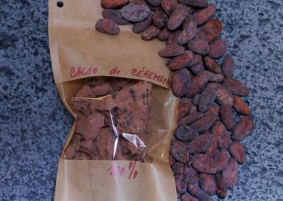 Sachet de cacao cérémoniel 100 % pur accompagné de fèves de cacao, posé sur un metate traditionnel en pierre de lave.