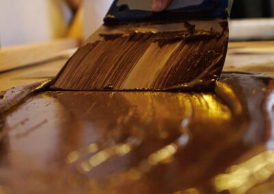 pâte de cacao fondue étalée sur une plaque de marbre à l’aide d’une spatule, pour créer une texture lisse et brillante.Tempérage du chocolat artisanal