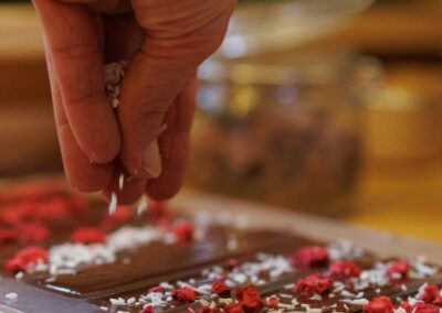 Main saupoudrant du chocolat noir fraîchement coulé avec copeaux de noix de coco, framboises lyophilisées et cardamome